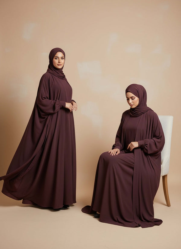 Woman wearing a long burgundy dress and hijab against a beige background